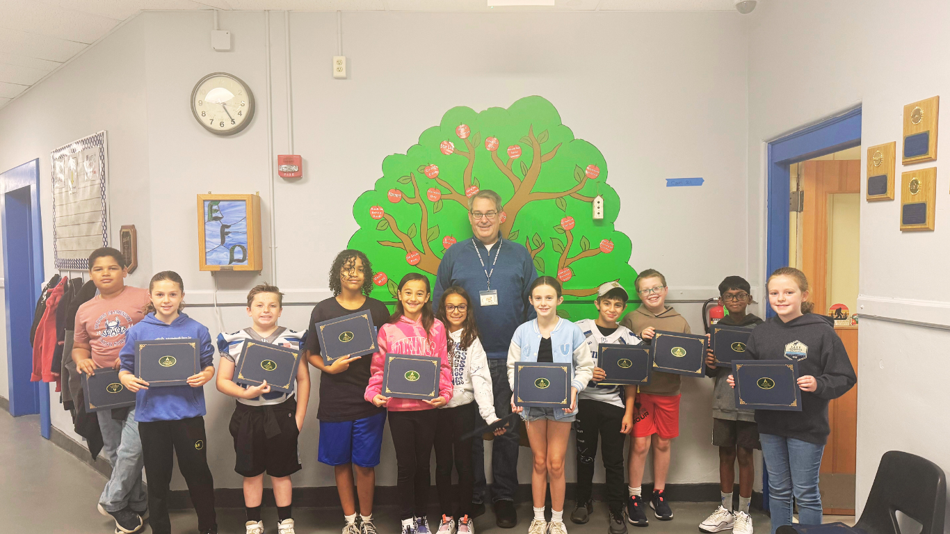 Group of students with the assistant principal of Walden ES holding certificates in front of a wall with a painting of a tree on it.