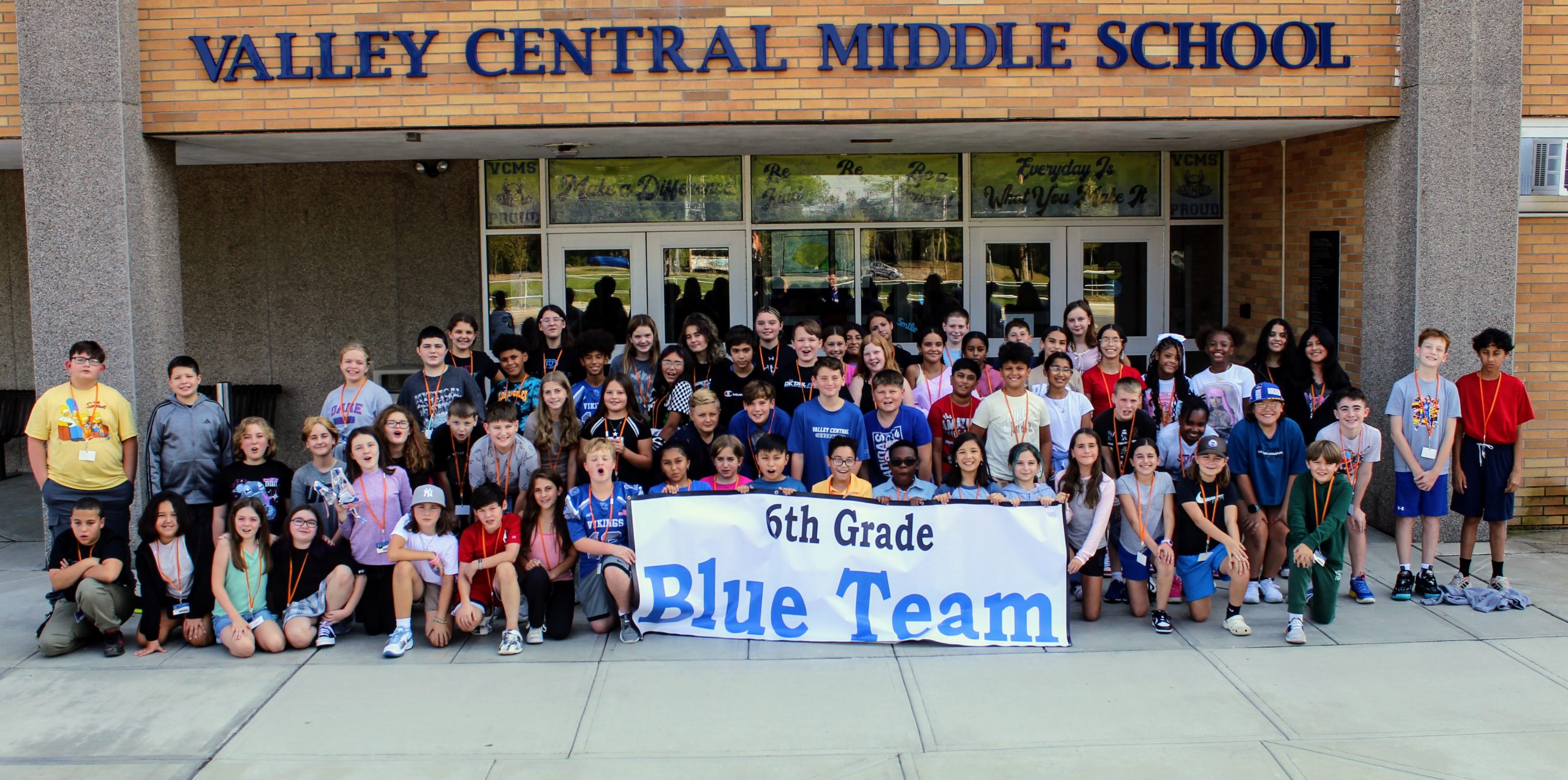 Group of middle school students standing outside the Valley Central Middle School with a banner in front of the first row of students that says 6th Grade Blue Team