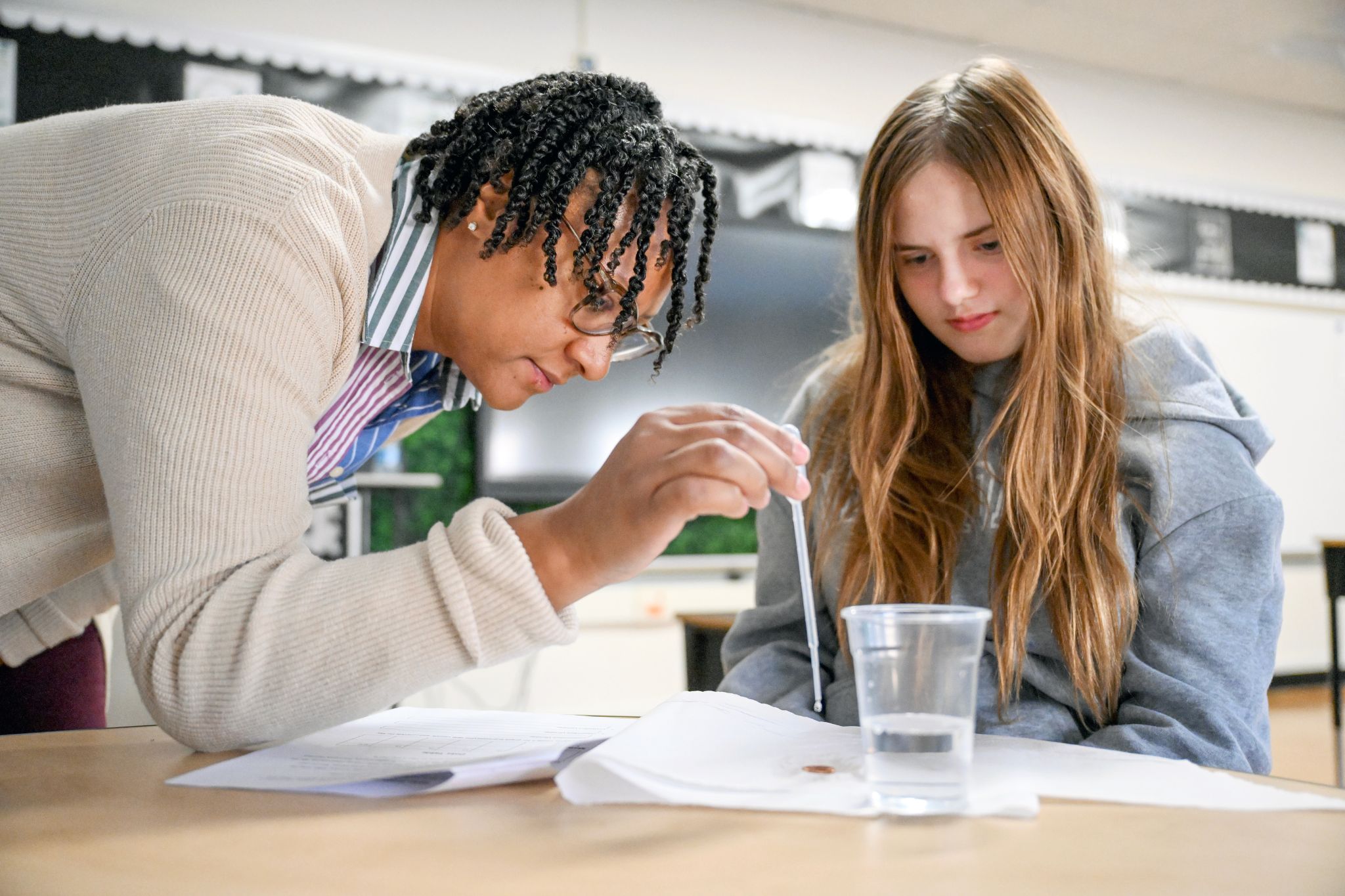 Two people work with a cup of water and a dropper at a desk.