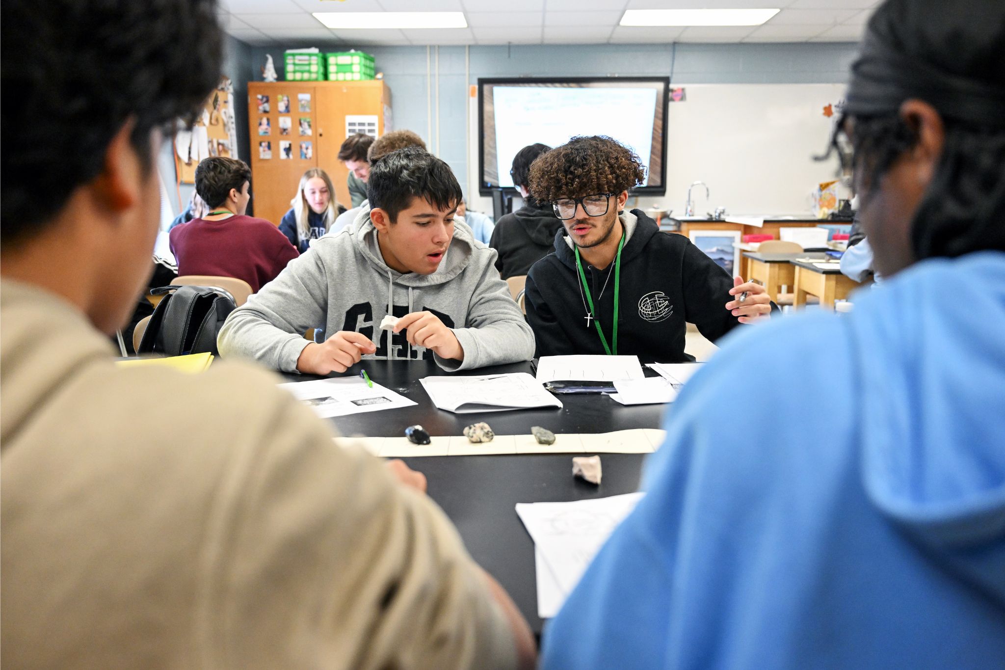 Four students sit at a table with papers and rocks.