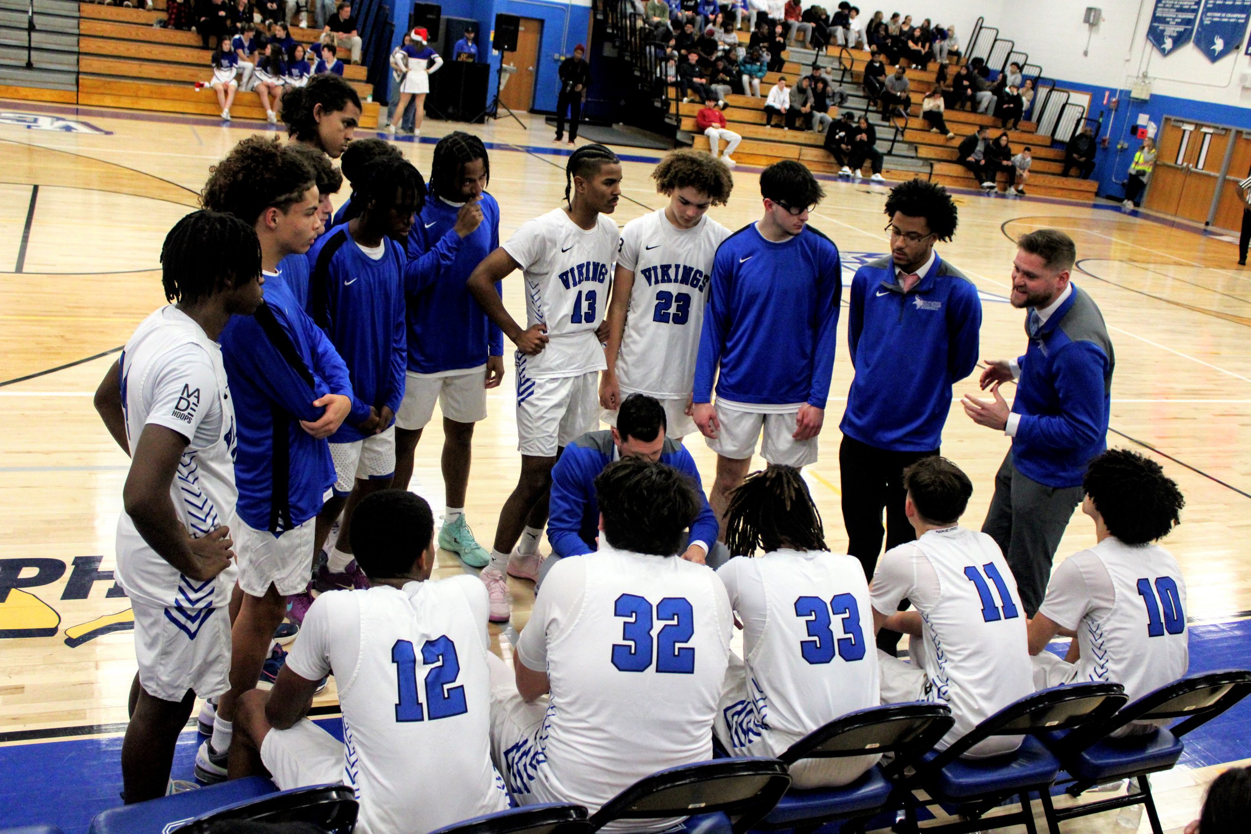 The boys basketball team sits on the bench and huddle around coach.