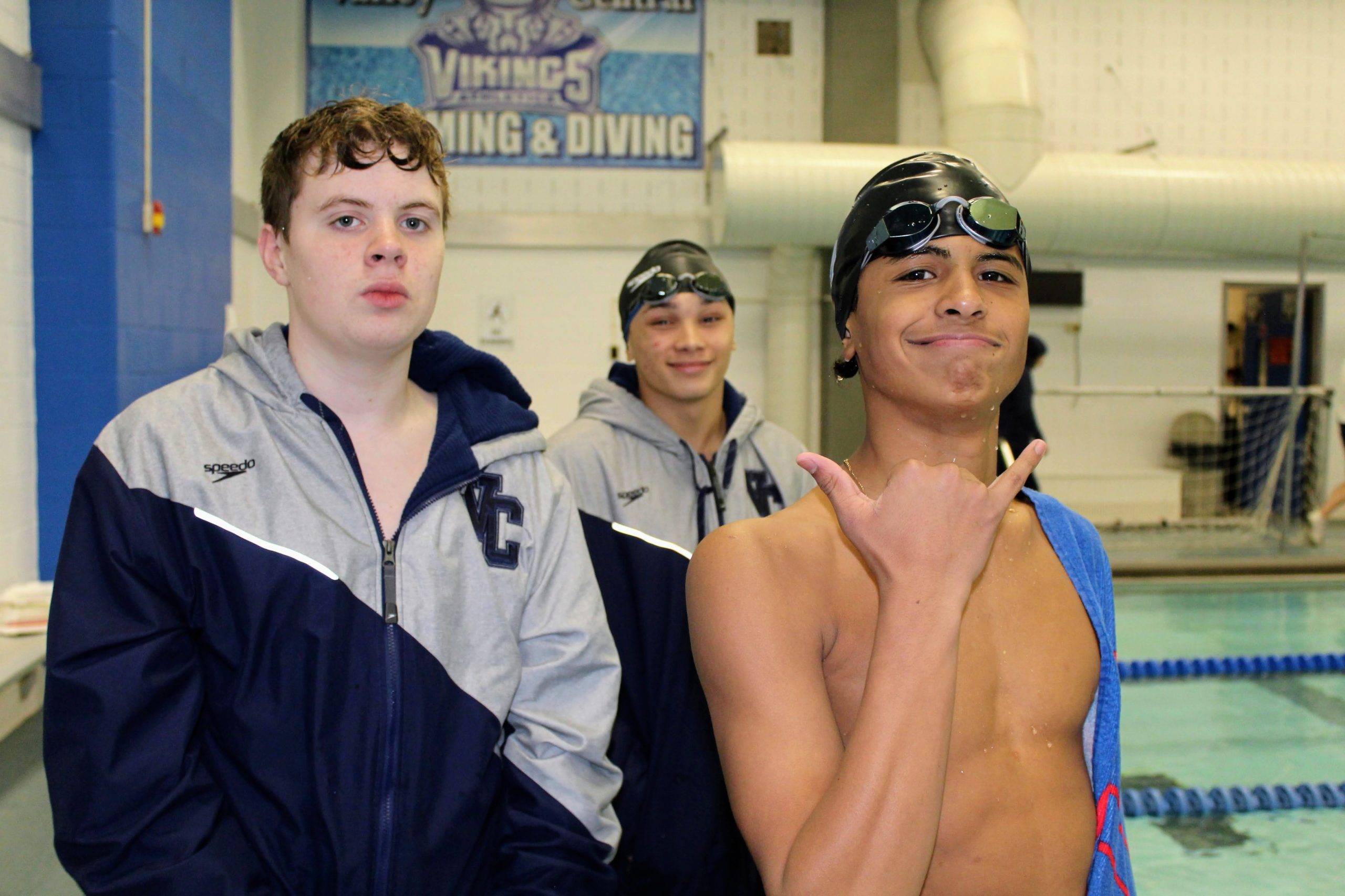 Three swimmers look and smile at the camera next to the pool.  