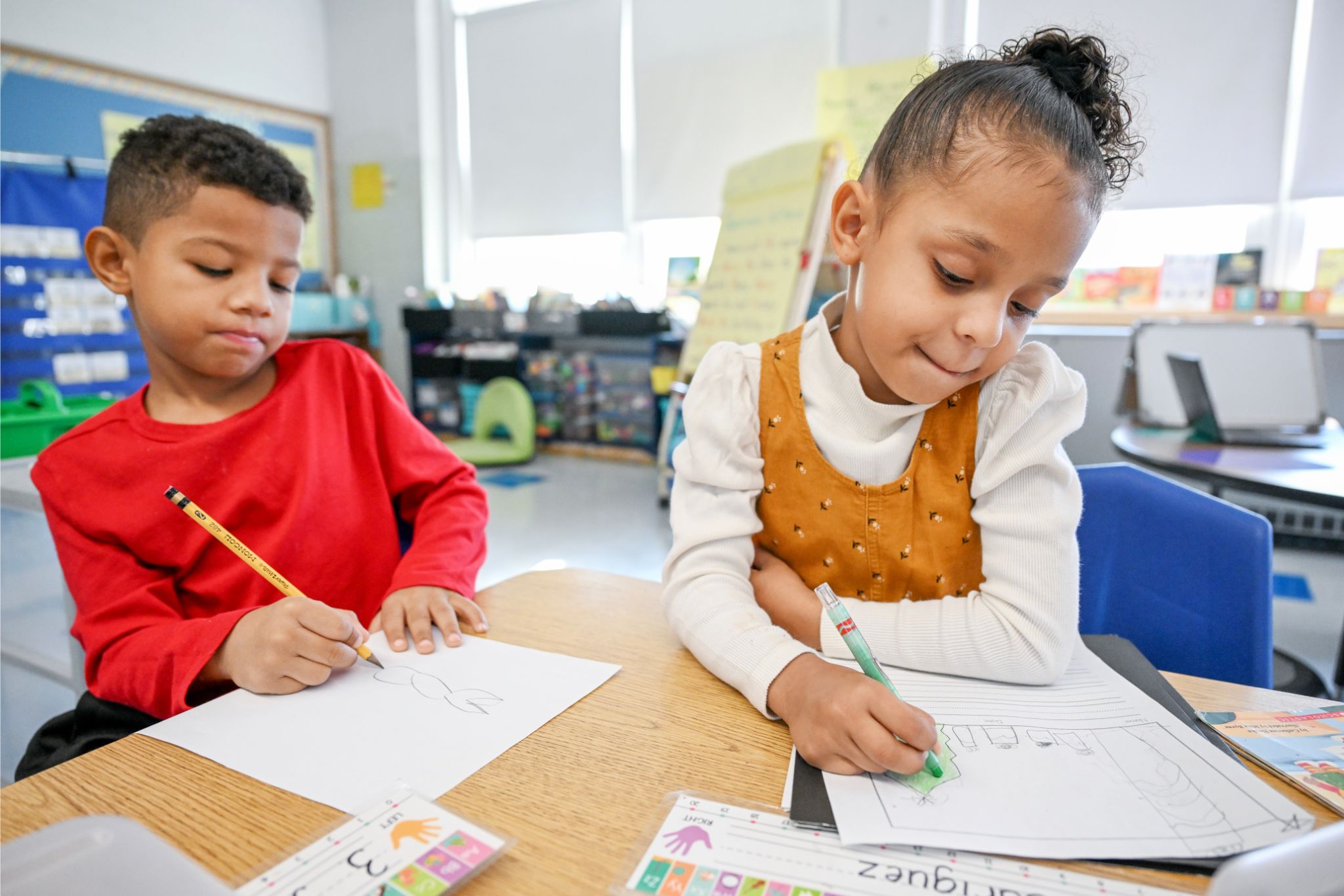 Two students writing on their papers at a table.